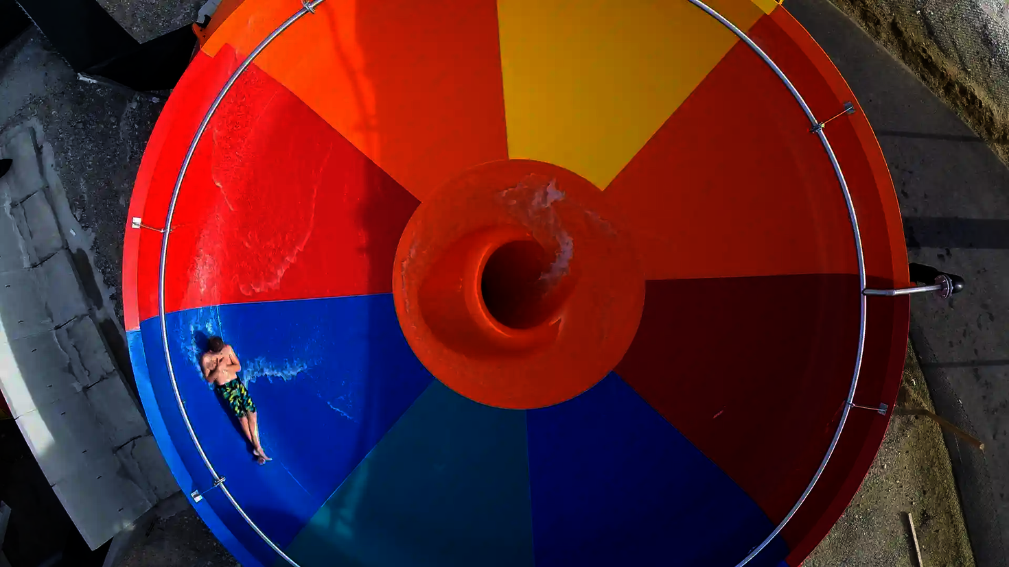 Obenansicht einer bunten Body Bowl Wasserrutsche, in der eine Person mit Badebekleidung rutscht.