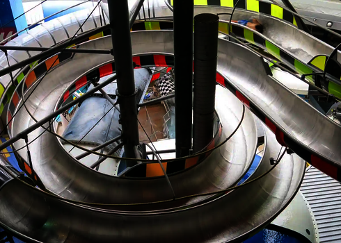 Spiralige Rutschverläufe mit silberner Oberfläche und gelb-schwarzem Muster im Tageslicht.