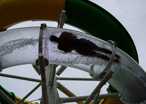 Eine Person rutscht durch eine transparente RR900, gelbe und grüne Rutschen im Hintergrund.