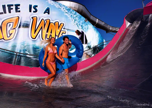 Ein Paar läuft lachend durch den Auslaufbereich der pinken Sidewinder-Rutsche im Außenbereich.