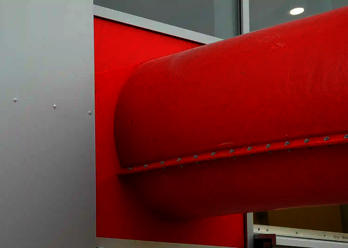 Rote Wasserrutsche durchstößt eine weiß-rote Gebäudefassade von innen nach außen.