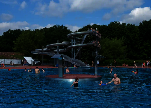 Schwimmbecken mit Badegästen, im Hintergrund ein Rutschenkomplex.