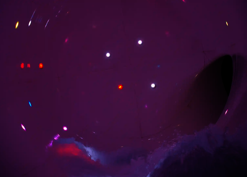 Innenansicht einer Wasserrutsche mit pinken LEDs und sprudelndem Wasser.