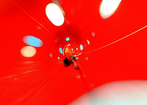 Eine rote Wasserrutsche von innen, mit einer rücklings rutschenden Frau.