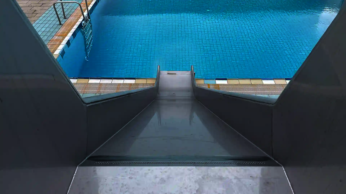 Die Kastenrutsche aus Edelstahl führt gerade in ein Schwimmbecken mit blauem Wasser.