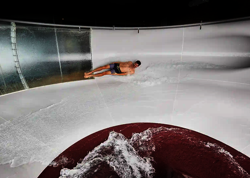 Innenansicht einer weißen Body Bowl Wasserrutsche, in der eine Person mit Badebekleidung rutscht.