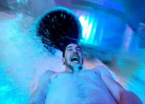 Nahaufnahme eines Mannes der in einem Wasserschwall eine Rutsche rutscht.