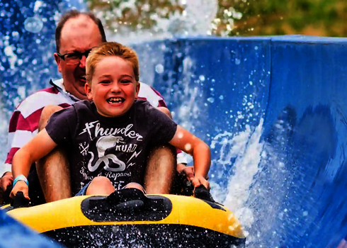Nahaufnahme von Vater und Kind in einem Rutschboot, spritzendes Wasser.