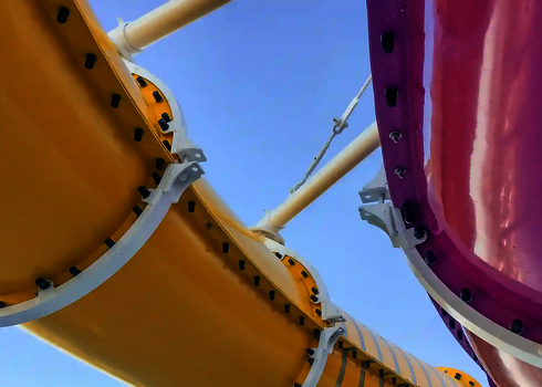 Zwei farbige Wasserrutschen in Gelb und Pink verlaufen nebeneinander vor blauem Himmel.