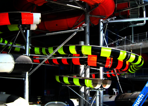 Body Racer Wasserrutschen in Rot, Gelb und Schwarz winden sich unter der Hallendecke.