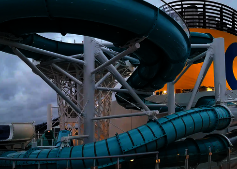 Hoch aufragende blaue 2-in-1 Racer Wasserrutsche mit gelbem Schornstein im Hintergrund.