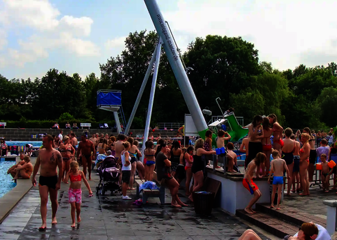 Viele Menschen in einem Schwimmbad, im Hintergrund ein grüner Cannonball.