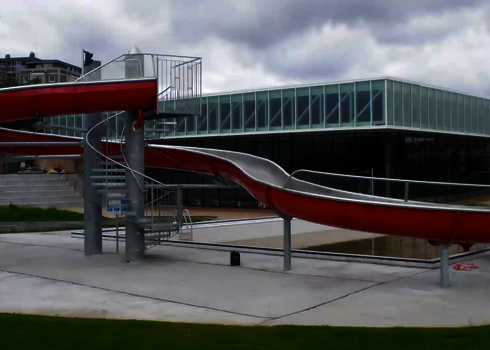 Niedrige WR1040-Rutsche mit Wendung und roter Außenverkleidung neben Hallenbad.