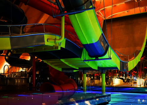 Seitliche Ansicht der Boomerang-Rutsche in Grün und Blau über dem beleuchteten Beckenbereich.