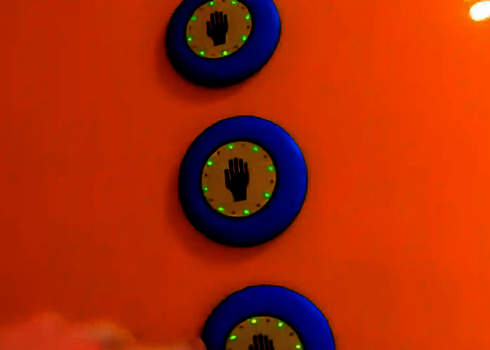 Drei blau-gelbe Auswahlknöpfe mit Hand-Symbolen leuchten grün an oranger Rutschenwand.