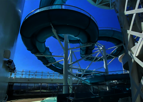 Blaue Spiralwasserrutsche auf dem Außendeck eines Kreuzfahrtschiffs bei Sonnenschein.