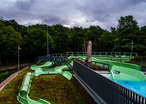 Grüner Wildwasserfluss mit Dachbegrünung und Brückenzugang in naturnaher Umgebung.