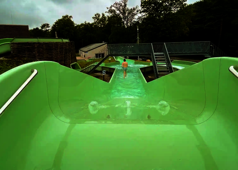 Grüner Wildwasserfluss mit leichtem Gefälle neben vor einer Brücke mit Treppenaufgang.