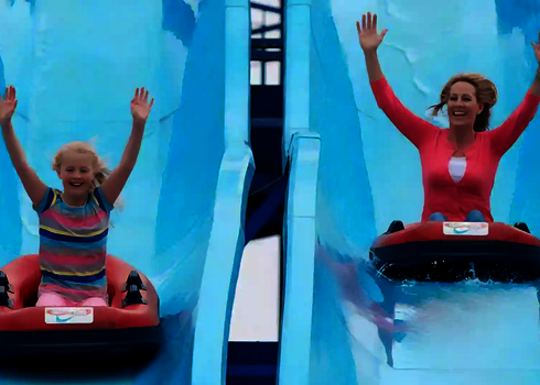 Zwei Personen rutschen lachend und mit erhobenen Händen parallel auf zwei Bahnen der Harakiri Wasserrutsche.