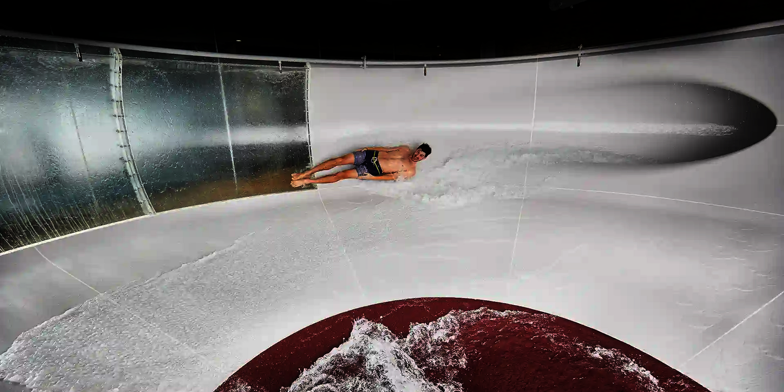 Mann rutscht in einer weißen Wasserrutsche mit einer großen Kurve und Glaswand