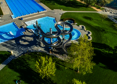 Überblick über Freibad mit WR1040-Rutsche, Liegewiese und Zugang zum See.