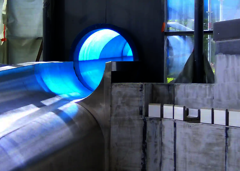 Blauer Röhrenrutschenauslauf endet erhöht in einem unfertigen Auffangbereich.