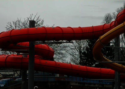 Rote geschwungene Röhrenrutsche getragen von Stahlstützen.