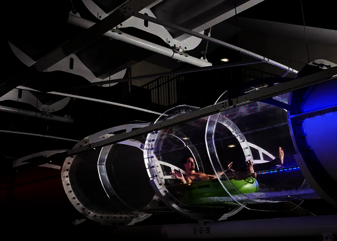 Ein Mann rutscht auf Reifen durch ein beleuchtetes Acryl-Element einer Wasserrutsche in dunklem Schwimmbad.