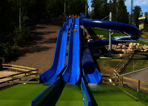 Freizeitpark mit unterschiedlichen blauen Rutschen, Personen stehen am Rand.