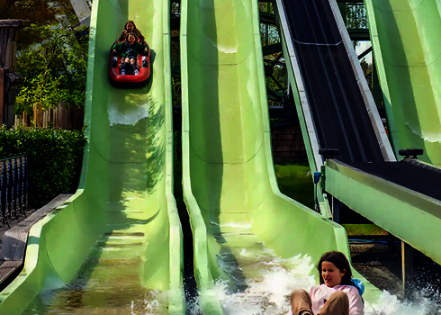 Nahaufnahme grüner Harakiri Wasserrutsche, zwei Personen im Boot sind am Rutschen.