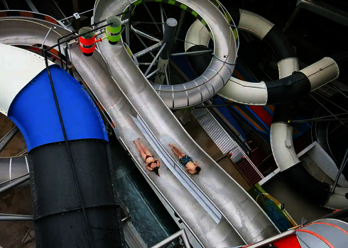  Zwei Personen rutschen nebeneinander auf einer breiten Body Racer Bahn im Wasserpark.