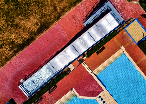 Vogelperspektive auf eine Breitwellenrutsche mit Auslaufbecken und ein blaues Schwimmbecken.