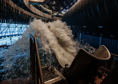 Wasserschwall kommt aus einem Cannonball vor dem Innenbereich eines Hallenbads.