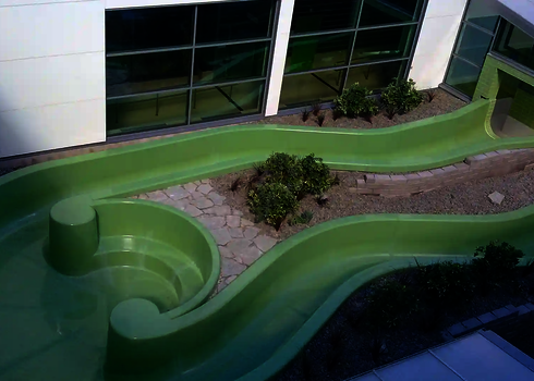 Grüner Wildwasserfluss mit geschwungenem Verlauf im begrünten Außenbereich eines Bads.