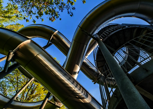 Blick von unten auf eine Edelstahl-Wasserrutsche, Stützen und Treppenaufgang.