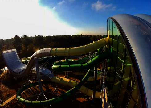 Blick von oben auf die Boomerang Rutsche und weitere, gelbe und grüne Wasserrutschen am Hallenbad.