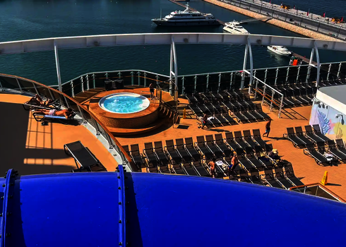 Blick auf das Decks eines Kreuzfahrtschiffes, mit einem Rutschenabschnitt und Liegestühlen im Hintergrund.