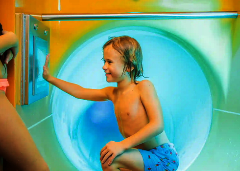 Junge kniet vor Rutscheneinstieg und wählt Rutschthema über Touchscreen aus.