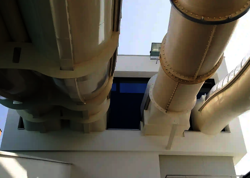 Mehrere helle Wasserrutschen verlassen dicht nebeneinander ein modernes Gebäude.