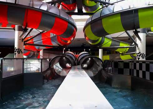 Auslaufbereich von zwei transparenten Rutschen mit Wasser, flankiert von rot-gelben Röhren.