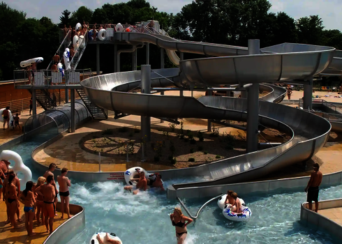 Wasserpark mit vielen Badegästen und einen Edelstahl-Rutschenkomplex in der Mitte.