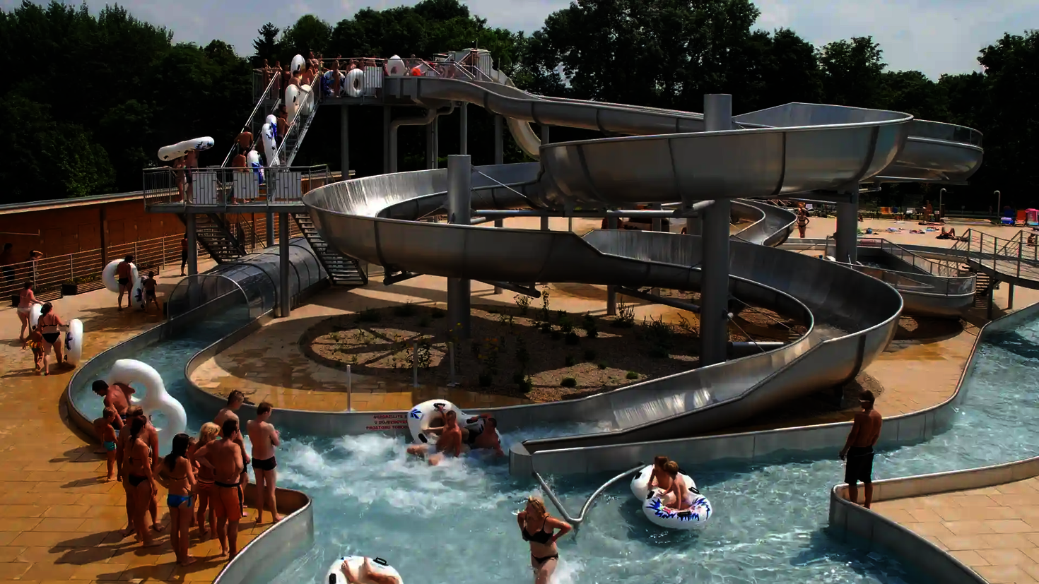 Wasserpark mit vielen Badegästen und einen Edelstahl-Rutschenkomplex in der Mitte.