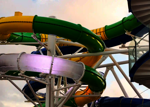 Mehrspurige Wasserrutschen in Gelb, Grün und Weiß winden sich an einem blauen Treppenturm entlang.