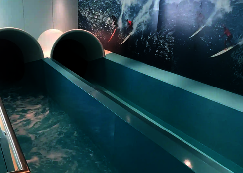 Two enclosed slide chutes end in a shallow blue pool with side railings.