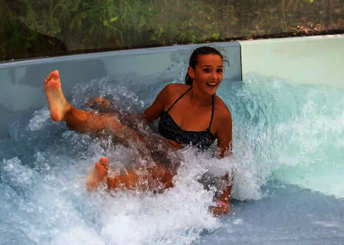 Eine junge Frau rutscht lachend durch das Auslaufbecken des Wildwasserflusses.