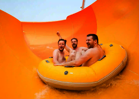 Drei Personen rutschen fröhlich auf einer gelben RR2700 Wasserrutsche auf einem gelben Rutschreifen.