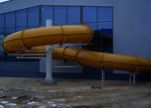 Gelbe Wasserrutsche verläuft von Gebäudefassade über schneebedeckten Boden.