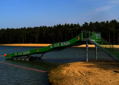 Eine grüne Breitwellenrutsche in einem Freibad mit einem See.