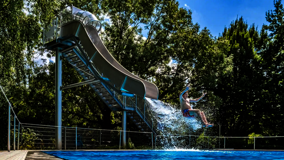 Ein Junge rutscht aus der Fallrutsche ins Becken und spritzt Wasser auf.