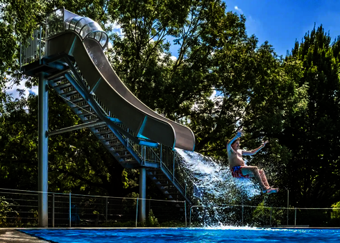 Ein Junge rutscht aus der Fallrutsche ins Becken und spritzt Wasser auf.